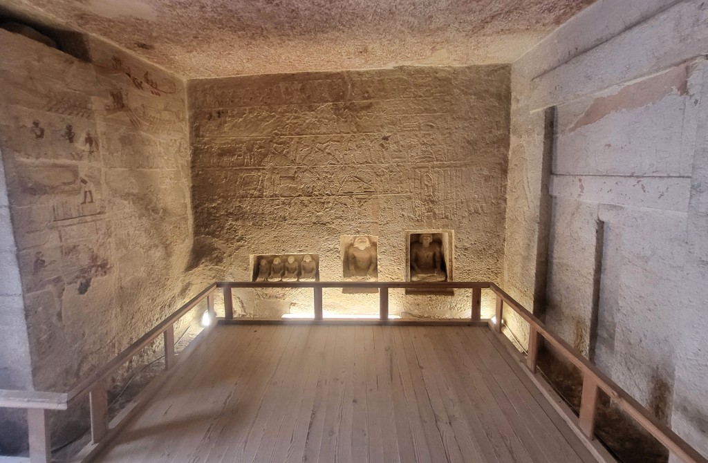 A tomb chamber with a false door in one wall, niches containing scribal statues facing and painted inscriptions on the rest. 