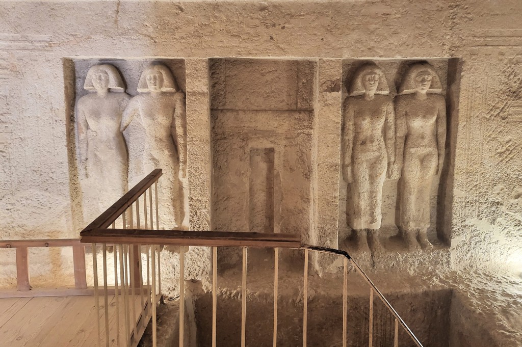 Behind a railing and staircase a false door, flanked by two pairs of engaged female statues are carved into the west wall of the offering chapel.